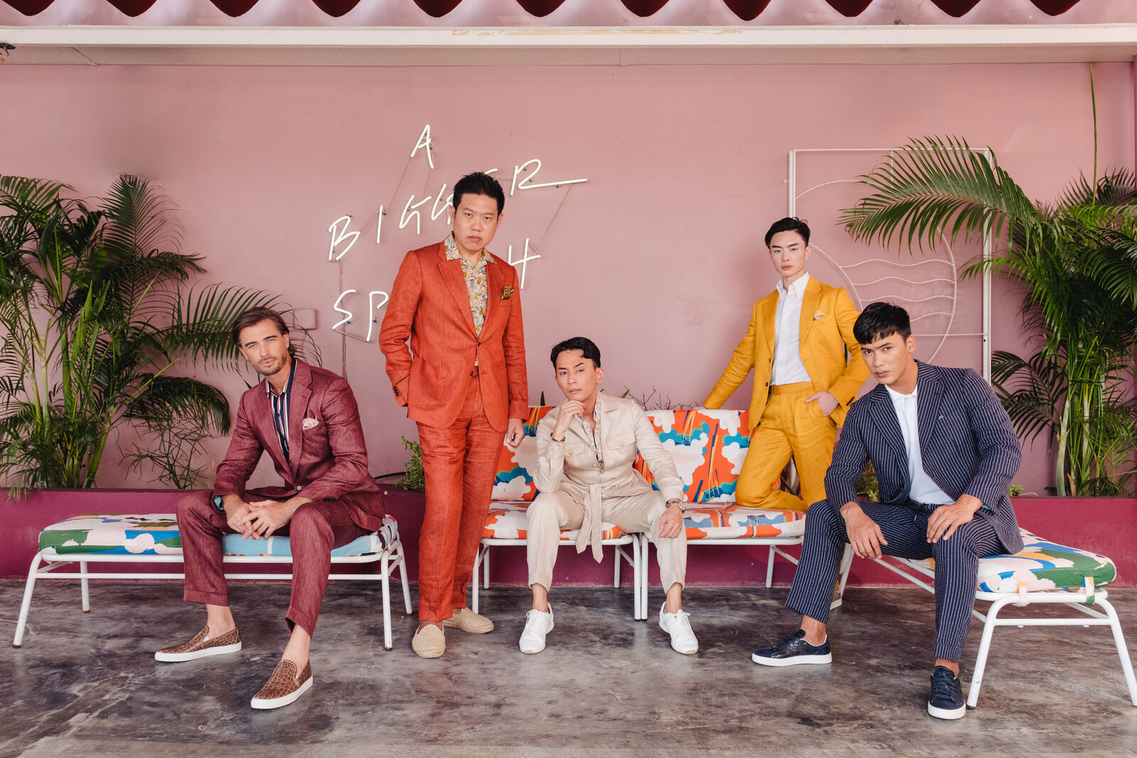 Five men in colourful tailored suits on a pink terrace