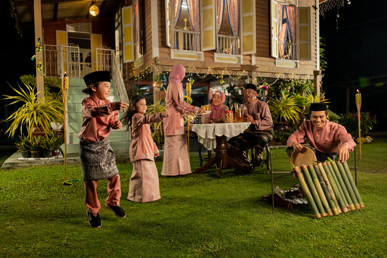 A family celebrating Hari Raya outside a kampung house at night, for Super Coffee